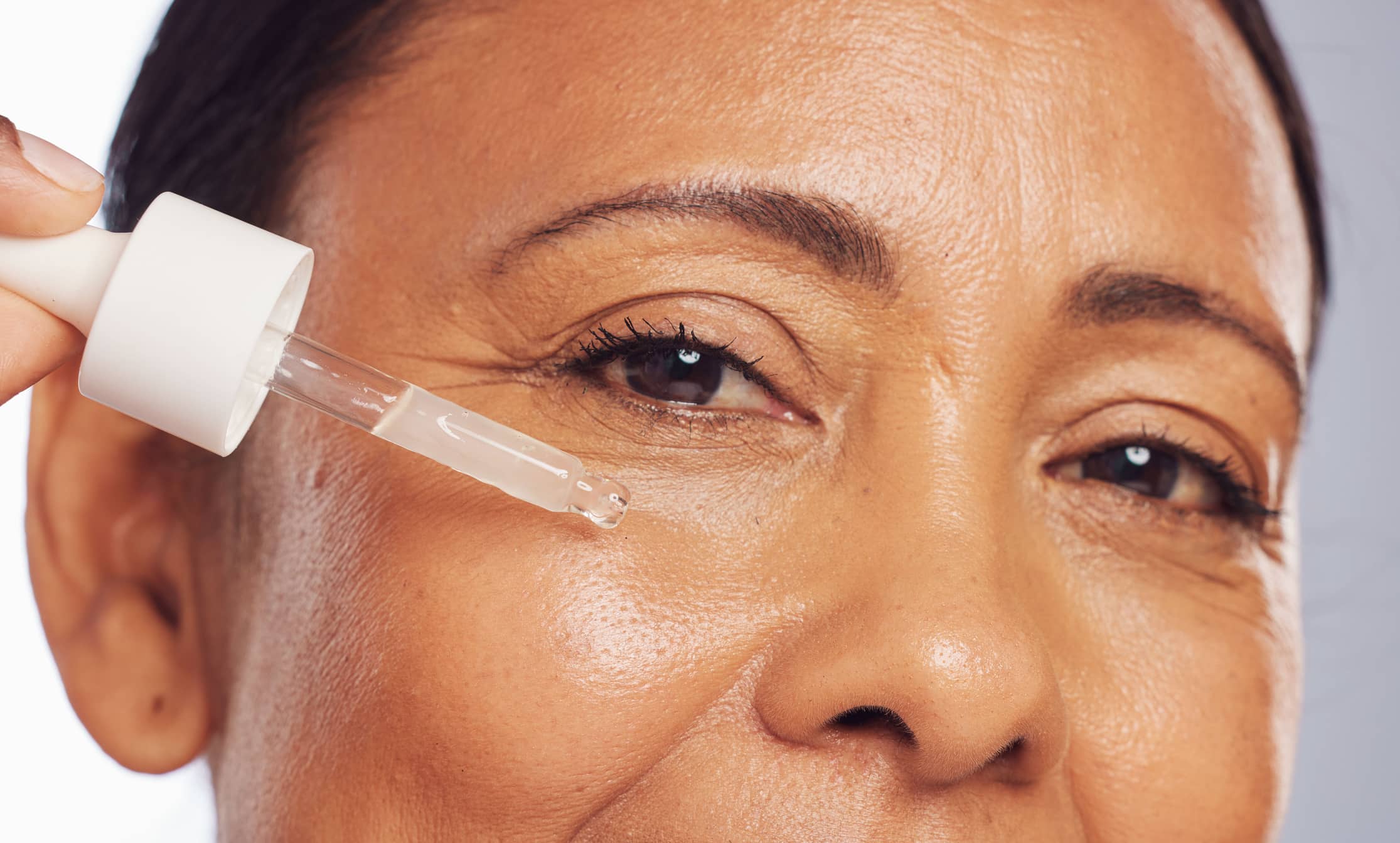 Woman, serum and portrait of face with dropper for beauty, aesthetic skincare or dermatology in studio. Closeup of mature female model, facial cosmetic oil and hyaluronic acid for collagen cosmetics